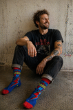 Man wearing colorful Sober AF socks sitting against a textured wall.