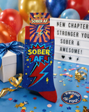 Sock with 'SOBER AF' design in front of balloons and motivational sign.