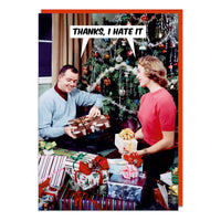 A Christmas card with a photo of a couple opening lots of presents in front of a big Christmas tree. They're both saying the same thing Thanks, I hate it.