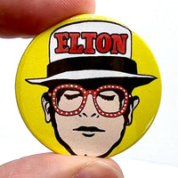 Elton John Pin Badge shows 1970s Elton John with straw boater